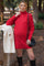 woman wearing a red maternity turtleneck sweater dress with a baby bump and holding a black crossbody bag