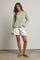 woman wearing a striped long sleeve sweater in turquoise and beige with white shorts and sandals