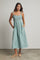 woman wearing a teal and white striped midi dress with smocked bodice and adjustable straps, standing with pockets