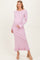 woman wearing a light pink ribbed maternity dress with long sleeves and ruffled hem, gently cradling her baby bump