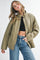 woman wearing a khaki quilted jacket over a black crop top and light blue high-waisted jeans
