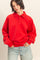 woman wearing a red oversized polo sweatshirt with a collar and three buttons, paired with light blue denim shorts