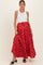 woman wearing a white tank top and a long red floral maternity skirt, gently holding her baby bump