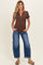 woman wearing a brown short sleeve maternity top with buttons and blue wide-leg jeans, showing her baby bump
