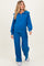 woman wearing a bright blue maternity zip-up hoodie and matching wide-leg pants, showcasing her baby bump
