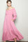 woman wearing a pink off-shoulder maxi dress with button details and ruffled hem, posing with one hand in pocket