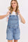 woman wearing a light blue denim overall shorts with a white cropped t-shirt underneath and smiling