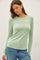 woman wearing a light green long sleeve fitted top with a round neckline and blue jeans