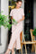 woman wearing a pink and white striped maxi dress with side slits, standing and holding flowers