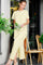 woman wearing a yellow and white striped maxi dress with side slits, standing next to plants in a cafe setting