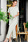 woman wearing a white and green striped maxi dress with side slits and a relaxed fit, standing and holding flowers
