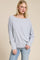 woman wearing a light gray oversized long sleeve top with a boat neckline and relaxed fit paired with blue jeans