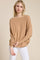 woman wearing a camel long sleeve oversized top with a boat neckline and relaxed fit paired with white pants