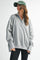 woman wearing a gray oversized pullover sweatshirt with a collared neckline and long sleeves, paired with black leggings and a green cap
