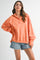 woman wearing an oversized coral pullover sweatshirt with a half-zip collar and paired with denim shorts