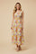 woman wearing a floral print maxi dress with smocked bodice and ruffle straps, standing on a beige background
