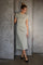woman wearing a sage green short sleeve midi dress with a side slit, posing against a textured gray background