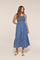 woman wearing a blue denim maxi dress with a smocked bodice and a flared ruffle hem
