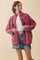 woman wearing a burgundy quilted jacket over a white crop top and denim shorts