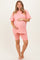 woman wearing a pink short sleeve maternity top and matching shorts, holding her baby bump