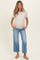 woman wearing a cream short sleeve maternity top with blue trim and light blue wide-leg jeans, holding her baby bump