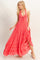 woman wearing a coral maxi dress with a halter neckline, tie detail, and ruffled hem