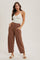 woman wearing a cream ribbed tank top and rust wide-legged pants, standing with one hand on her hip