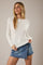 woman wearing a white long sleeve top and a denim mini skirt, posing with one hand on her hip