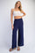 woman wearing a white crop top and navy wide-leg pants, standing with one hand on her hip
