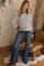 woman wearing a black and white striped maternity top with long sleeves and blue flare jeans, posing indoors