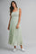 woman wearing a light green sleeveless maxi dress with tie shoulder straps and pleated skirt, standing against a grey background