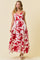woman wearing a white maxi dress with red floral print and spaghetti straps, standing against a light background