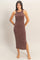 woman wearing a brown ribbed midi dress with a side slit, standing barefoot against a neutral background
