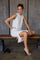 woman wearing a light gray sleeveless midi dress with side slits, seated on a bench in a casual pose