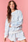 woman wearing a light blue floral print sweatshirt with white stripes and matching ruffled shorts on a pink background