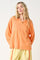 woman wearing an oversized orange long sleeve top with a relaxed fit and light yellow pants