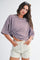 woman wearing a purple and brown striped oversized t-shirt with knotted detail, paired with beige shorts and sunglasses on her head