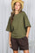 woman wearing an olive green oversized t-shirt with short sleeves and brown shorts, accessorized with a straw hat