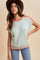 woman wearing a light mint green short sleeve knit top with coral detailing and a brown hat