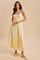 woman wearing a yellow maxi dress with lace detailing and a tiered skirt, standing against a neutral background