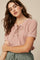 woman wearing a light pink short sleeve top with a lace-up neckline and rolled cuffs