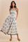 woman wearing a white floral maxi dress with adjustable straps and pockets, standing against a neutral background
