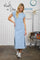 woman wearing a light blue maxi dress with short sleeves and side slits, standing in a laundry-themed setting