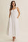 woman wearing a white maxi dress with a square neckline, buttons, and pockets, styled with strappy sandals