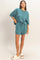 woman wearing a teal oversized sweatshirt and matching shorts with a drawstring, paired with cream slide sandals