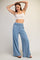 woman wearing a light blue high-waisted wide leg pants and a white crop top, posing with her hands above her head