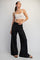 woman wearing a white cropped tank top and black wide-leg pants, posing with one hand on her hip