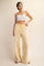 woman wearing a white cropped top and light yellow wide-leg pants, standing with one hand on her hip