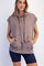 woman wearing a taupe sleeveless hoodie with a front pocket and tie detail, paired with navy bike shorts
