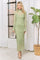 woman wearing a sheer green long sleeve dress with white polka dots and a high neck standing by a window